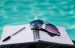 sunglasses and a pen sitting on a notebook next to a swimming pool