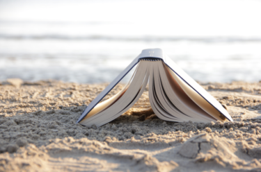 book lying face down on a sandy beach with the ocean in the background
