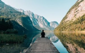 A person sitting on a dock by a lake, with mountains in the background. #How I Got Over Imposter Syndrome #what is imposter syndrome #definition of imposter syndrome #how to use positive affirmations #how do you write positive affirmations