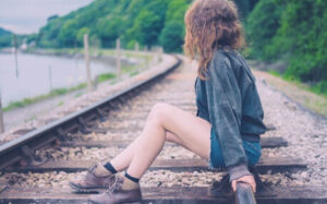 woman sitting on railroad tracks, representing the wrong side of the tracks trope