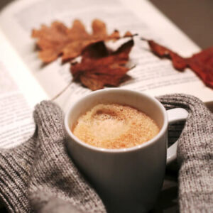 cocoa, open book, hands of someone wearing a sweater 