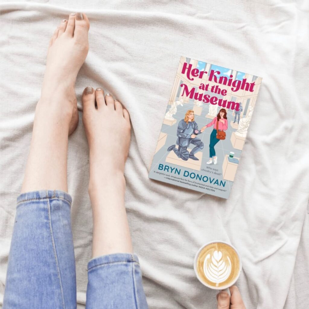 the paperback of Her Knight at the Museum by Bryn Donovan, next to a woman in bed with latte, jeans, bare feet