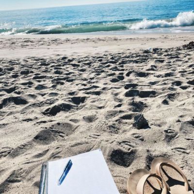 notebook, pen, and sandals on a beach