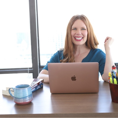 author Bryn Donovan sitting at desk in front of laptop, smiling at you