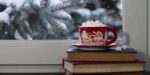 christmas mug, books, window, snow on pines outside