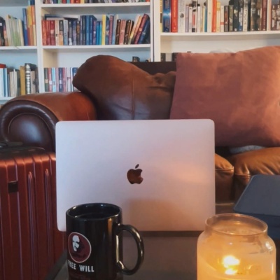 laptop, candle, couch, mug, fantasy novels on shelves in background